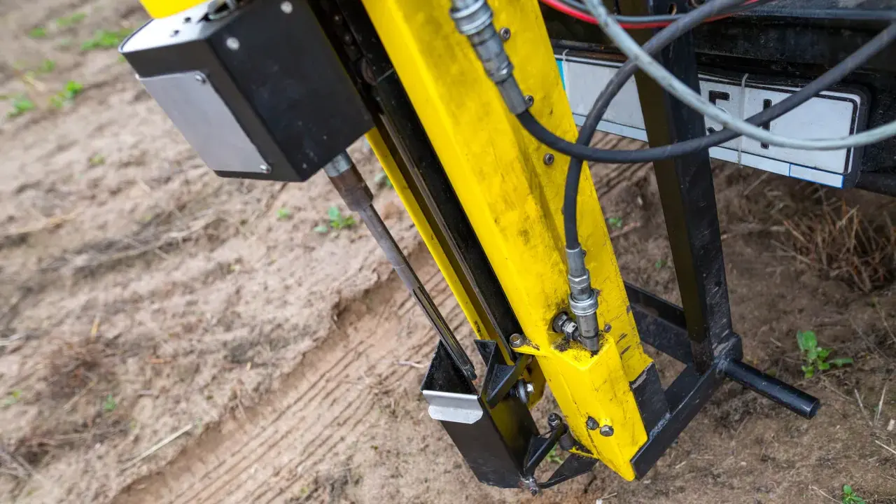 Żółta maszyna do badań geotechnicznych gruntu w akcji. Wiertło zagłębia się w ziemię, zbierając próbki do analizy.