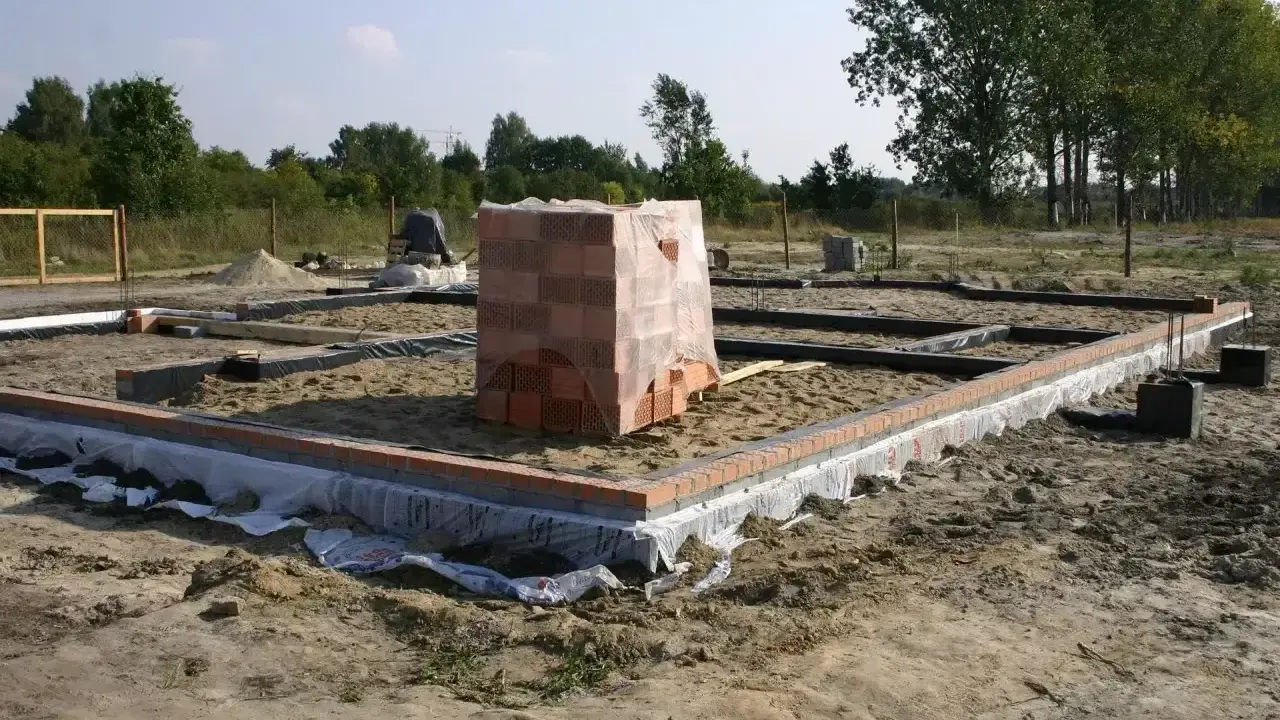 Stan zero budynku: fundamenty z cegły i betonu, stos materiałów budowlanych.