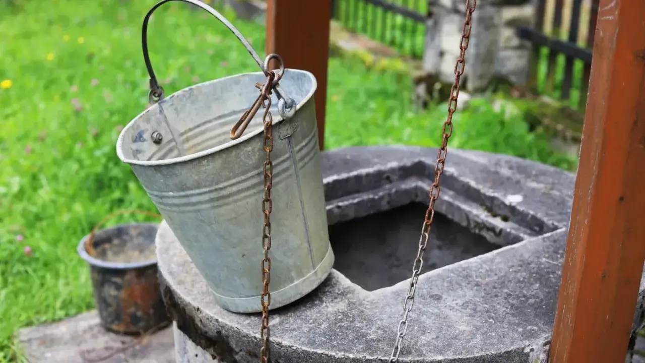 Metalowy wiaderko przy studni, gotowe do pracy. Ktoś zastanawia się, jak wykopać studnię, by mieć własne źródło wody.
