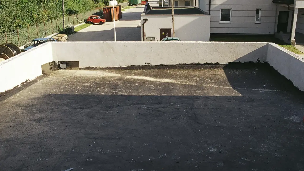Płaski dach z widocznym systemem odwodnienia. W tle budynki i drzewa.