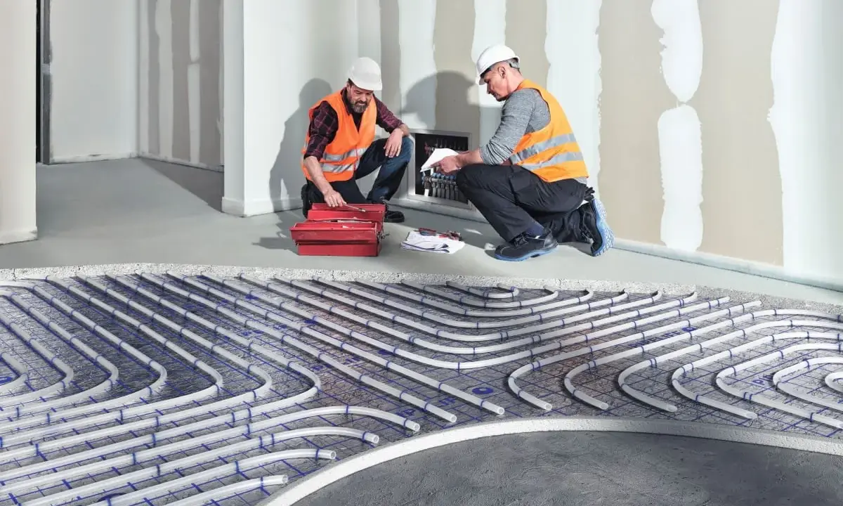 Dwóch fachowców montuje instalację ogrzewania sufitowego wodnego. Rury systemu ułożone są na siatce.