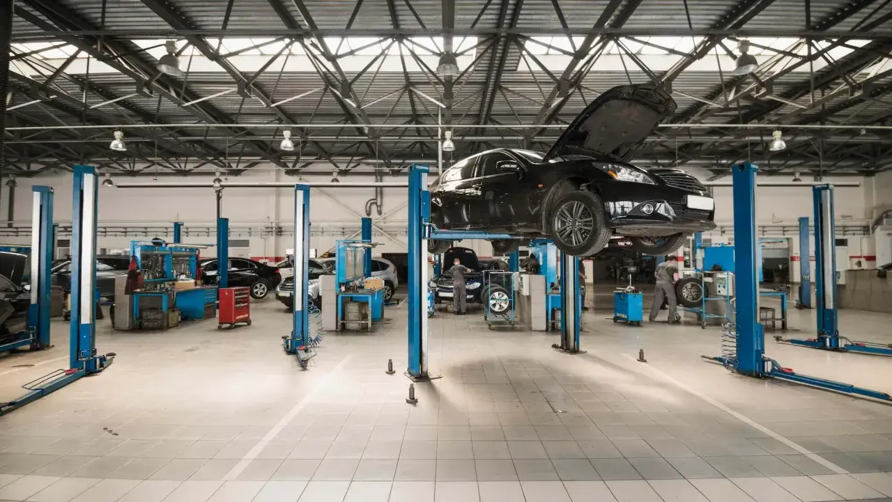 Nowoczesny projekt warsztatu samochodowego. Na podnośnikach stoją auta, mechanicy pracują.