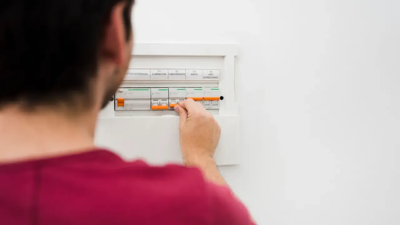 Mężczyzna manipuluje wyłącznikami w skrzynce elektrycznej, co może być związane z tym, jak obliczyć zużycie prądu.