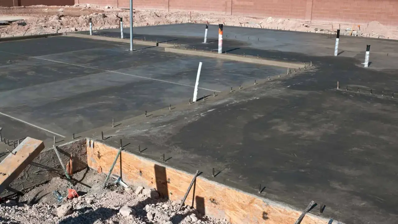 Świeżo wylany betonowy fundament z widocznymi rurami i zbrojeniem. Ziemia wokół czeka na materiał, czym obsypać fundamenty z zewnątrz.