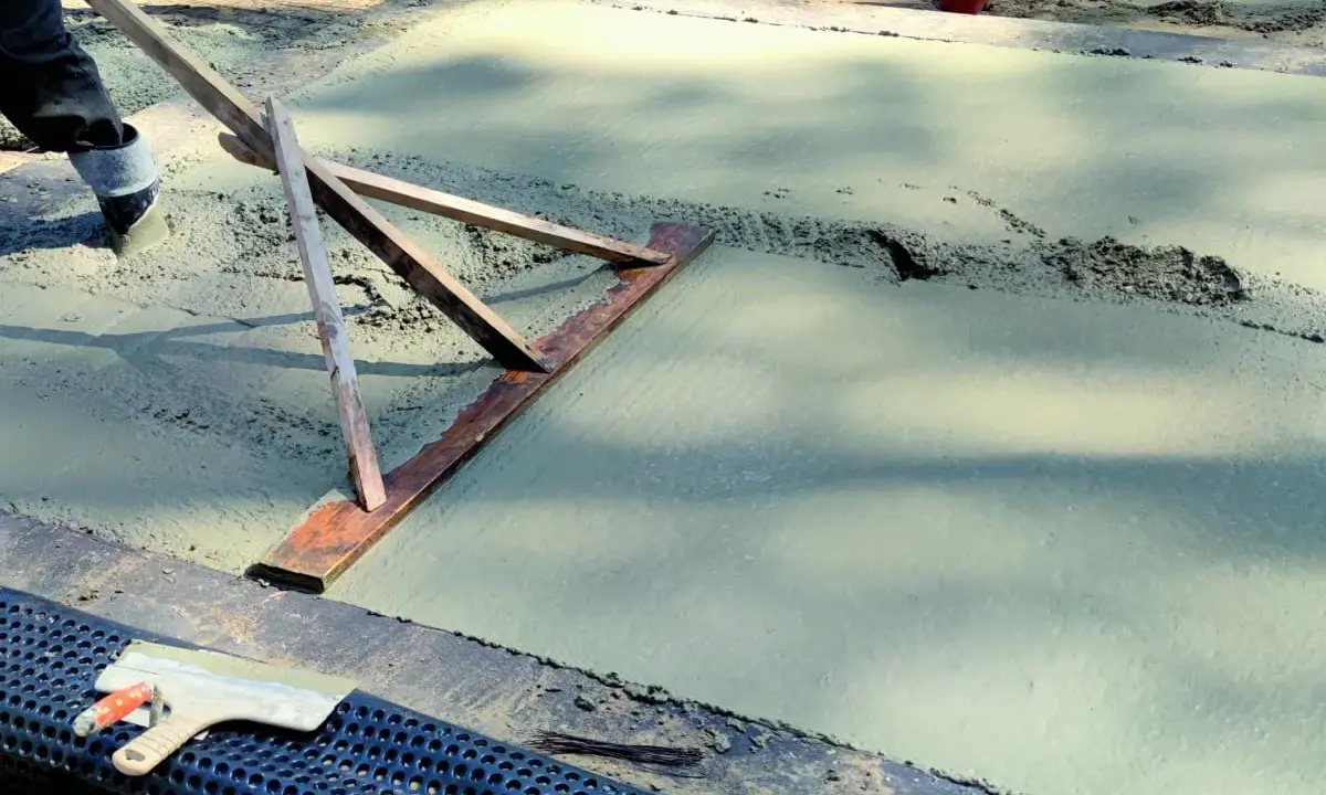 Pracownik wyrównuje świeży beton, sprawdzając, jaka grubość chudziaka jest potrzebna. Narzędzie do zacierania betonu w akcji.