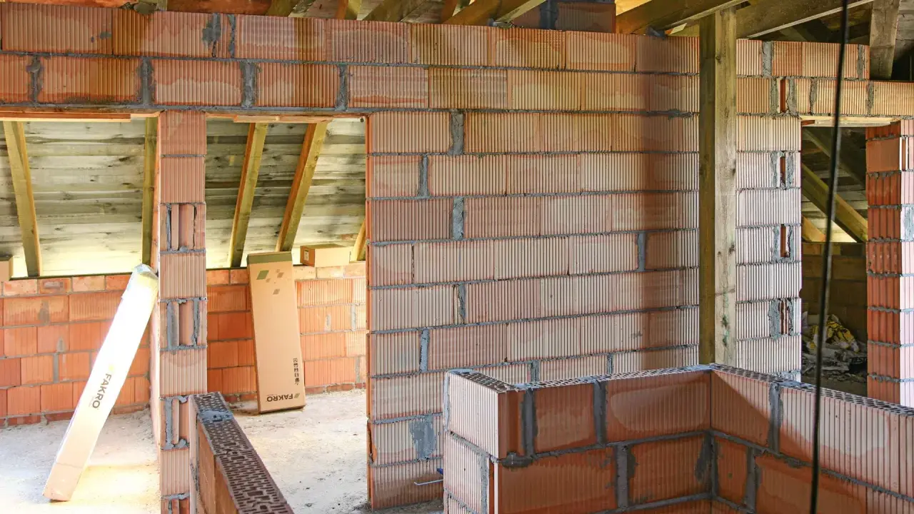 Niedokończone ściany z pustaków ceramicznych, widoczne drewniane belki stropowe. Wady murowania na piankę mogą prowadzić do problemów.