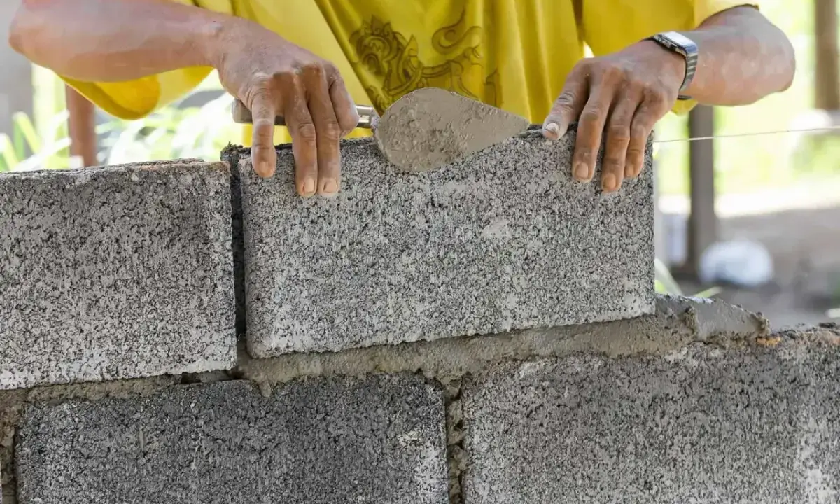 Murarz kładzie betonowy bloczek na zaprawie, używając kielni.