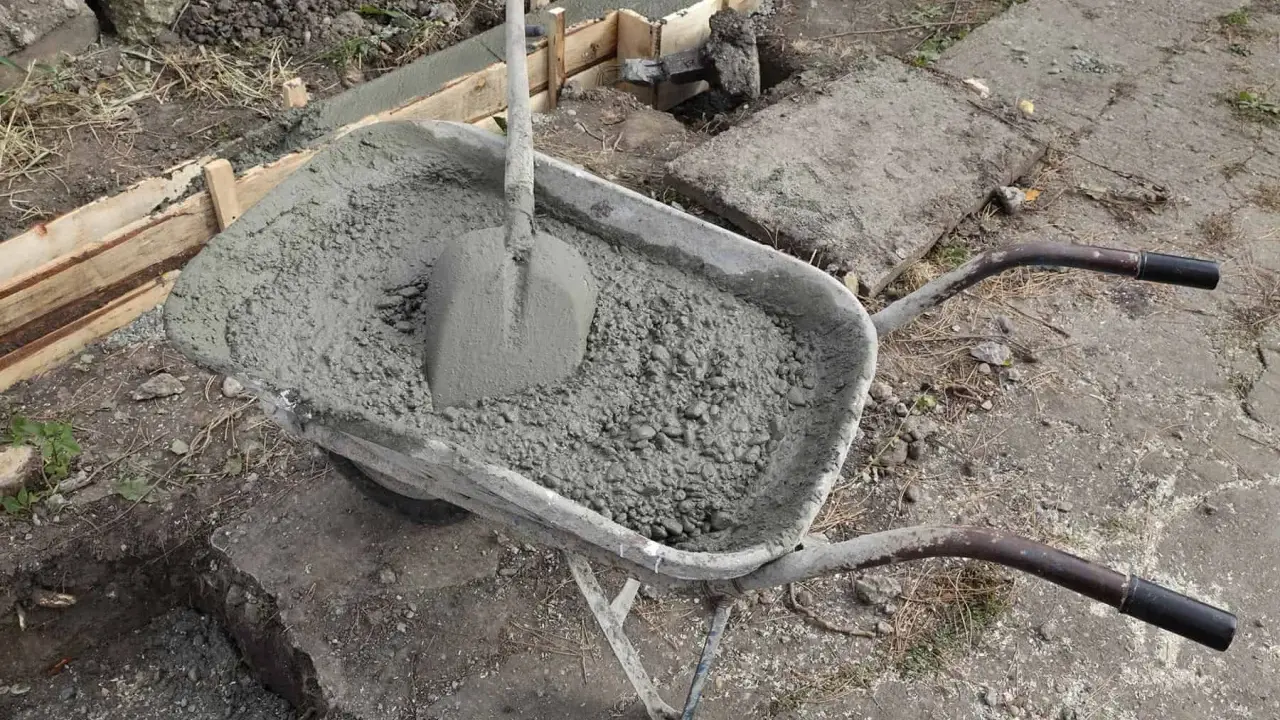 Taczka z betonem i łopatą czeka na wylanie zbrojenia ławy fundamentowej.