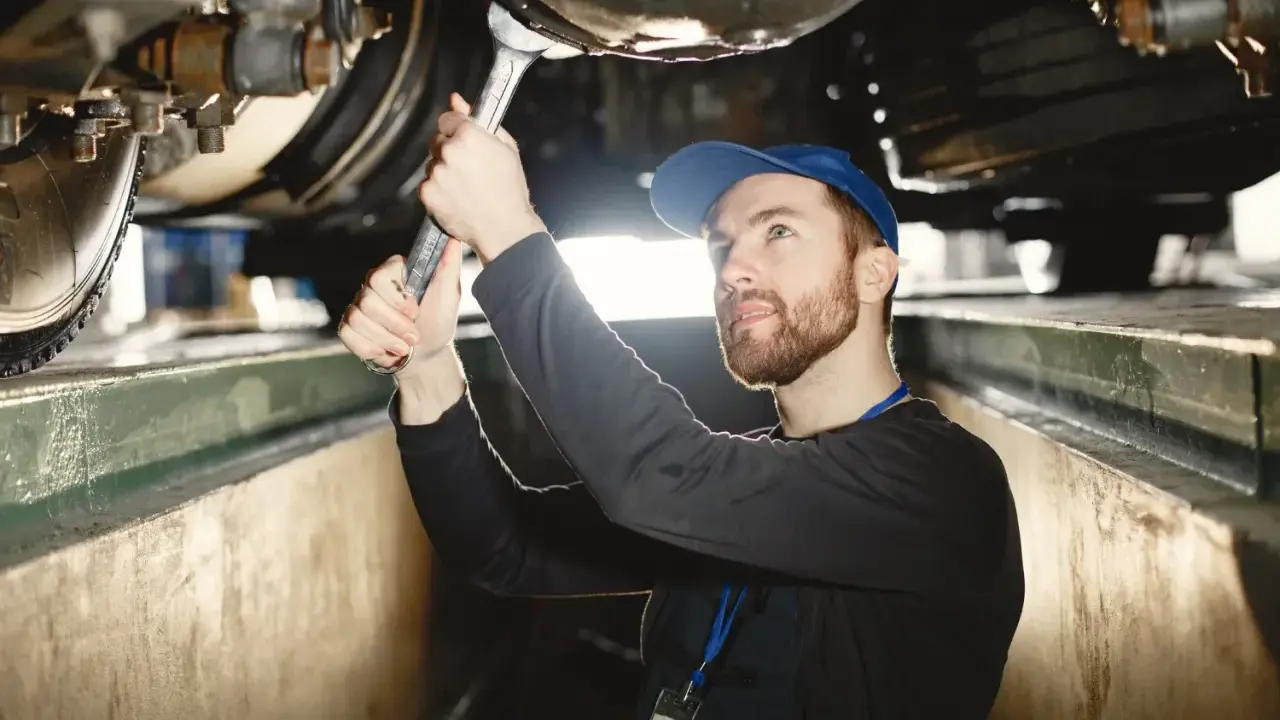 Mechanik z kluczem pracuje pod samochodem, sprawdzając wymiary kanału samochodowego.