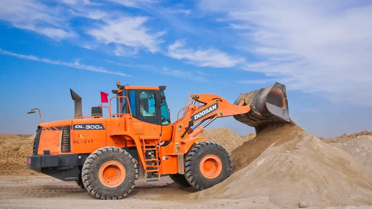 Pomarańczowa ładowarka Doosan DL300A zasypuje kopiec piasku, który może posłużyć jako żwir do betonu.