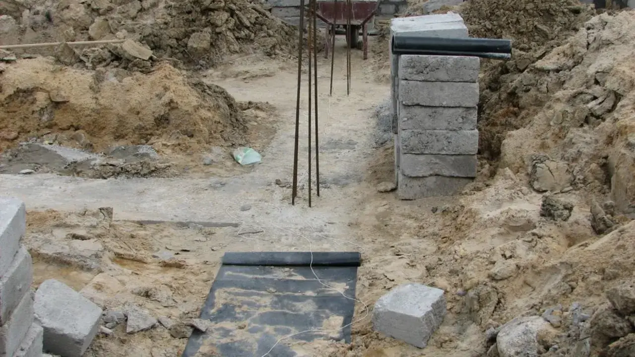 Budowa fundamentu z bloczków betonowych, zbrojenie i wózek widłowy w tle.