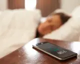 Telefon na stoliku nocnym pokazuje 7:30, budząc śpiącą osobę. To typowy widok na poziomie zero budynku, gdzie zaczyna się dzień.