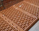 Czerwone pustaki ceramiczne ułożone obok siebie, z siatką zbrojeniową w tle. Zastanawiasz się, ile pustaków na m2 potrzeba do budowy?