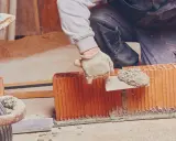 Murarz nakłada zaprawę murarską na pustaki, dbając o właściwe proporcje mieszanki.