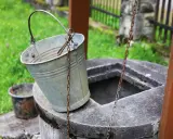 Metalowy wiaderko przy studni, gotowe do pracy. Ktoś zastanawia się, jak wykopać studnię, by mieć własne źródło wody.