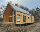 Nowoczesne domy modulowe bez pozwolenia, z drewnianą elewacją i dużymi oknami, stoją na skraju lasu.