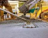 Pracownik wylewa beton, wyrównując go narzędziem. W tle koparka. Beton można lać do ok. 30°C.