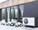 Nowoczesny dom w zimowej scenerii. Obok budynku stoi biała jednostka, która może być alternatywą dla pompy ciepła.