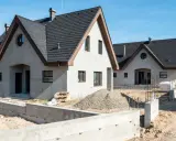 Nowe domy z betonu w budowie, z ciemnymi dachami i jasnymi ścianami, na tle błękitnego nieba.