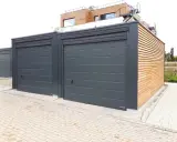 Nowoczesny garaż z płyt ogrodzeniowych, z drewnianą elewacją i szarymi bramami.