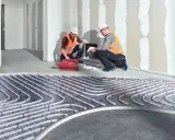 Dwóch fachowców montuje instalację ogrzewania sufitowego wodnego. Rury systemu ułożone są na siatce.