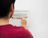 Mężczyzna manipuluje wyłącznikami w skrzynce elektrycznej, co może być związane z tym, jak obliczyć zużycie prądu.