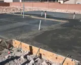 Świeżo wylany betonowy fundament z widocznymi rurami i zbrojeniem. Ziemia wokół czeka na materiał, czym obsypać fundamenty z zewnątrz.