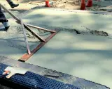 Pracownik wyrównuje świeży beton, sprawdzając, jaka grubość chudziaka jest potrzebna. Narzędzie do zacierania betonu w akcji.