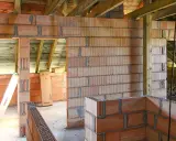 Niedokończone ściany z pustaków ceramicznych, widoczne drewniane belki stropowe. Wady murowania na piankę mogą prowadzić do problemów.