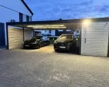 Nowoczesna wiata na 2 samochody projekt. Dwa czarne auta, Tesla i Lexus, stoją pod zadaszeniem z oświetleniem LED.