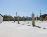 Plac budowy z betonową płytą i słupami betonowymi konstrukcyjnymi. W tle budynek i dźwig.