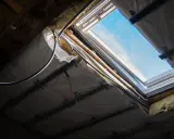 Trwa wymiana okna dachowego. Widoczne elementy konstrukcji, izolacja i przewody elektryczne.