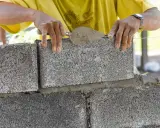 Murarz układa bloczek betonowy, dbając o jego wymiary i równość.
