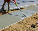 Pracownik wygładza świeży beton na chodniku. Jaki beton na wieniec? Ten budowlany jest idealny do takich prac.