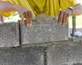 Murarz kładzie betonowy bloczek na zaprawie, używając kielni.