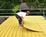 Pracownik układa płyty izolacyjne na dachu płaskim. Zapewnia to skuteczną izolację termiczną budynku.