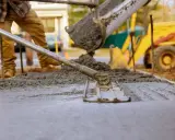 Pracownik wylewa beton, który będzie długo schnął w temperaturze 5 stopni. W tle koparka.