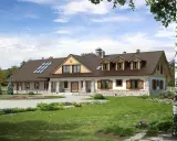 Projekt pensjonatu 10 pokoi. Dom z kamienną podmurówką, drewnianymi okiennicami i lukarnami, otoczony zielenią.