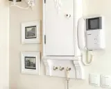 Biała zabudowa skrzynki elektrycznej w przedpokoju, z wieszakami na klucze i domofonem.