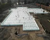 Szalunek płyty fundamentowej gotowy do zalania betonem. Na białej piance izolacyjnej ułożono zbrojenie i rury.