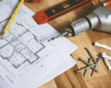 Narzędzia budowlane i plan mieszkania. Zastanawiasz się, jak obliczyć metry kwadratowe ściany? Ten obrazek pokazuje, że potrzebujesz planu i miarki.