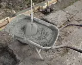 Taczka z betonem i łopatą czeka na wylanie zbrojenia ławy fundamentowej.