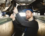 Mechanik z kluczem pracuje pod samochodem, sprawdzając wymiary kanału samochodowego.