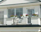 Białe okna pięknie komponują się z jasną, tynkowaną elewacją, tworząc elegancki wygląd. Balkon ozdobiony kwiatami dodaje uroku.