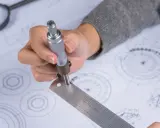 Ręka trzymająca suwmiarkę nad rysunkiem technicznym, pokazując jak czytać rysunek techniczny.