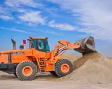 Pomarańczowa ładowarka Doosan DL300A zasypuje kopiec piasku, który może posłużyć jako żwir do betonu.