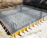 Gotowe zbrojenie ławy fundamentowej 40x60, otoczone drewnianym szalunkiem, czeka na zalanie betonem.