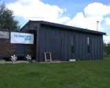 Mobilny garaż na zgłoszenie, z banerem "Zbuduj sam dom", stoi na trawie.