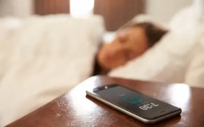 Telefon na stoliku nocnym pokazuje 7:30, budząc śpiącą osobę. To typowy widok na poziomie zero budynku, gdzie zaczyna się dzień.