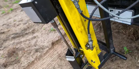 Żółta maszyna do badań geotechnicznych gruntu w akcji. Wiertło zagłębia się w ziemię, zbierając próbki do analizy.